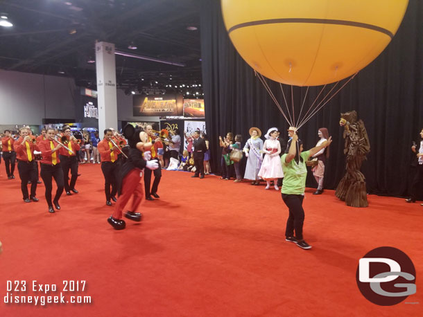 Mickey leads a band following the cast members with balloons.