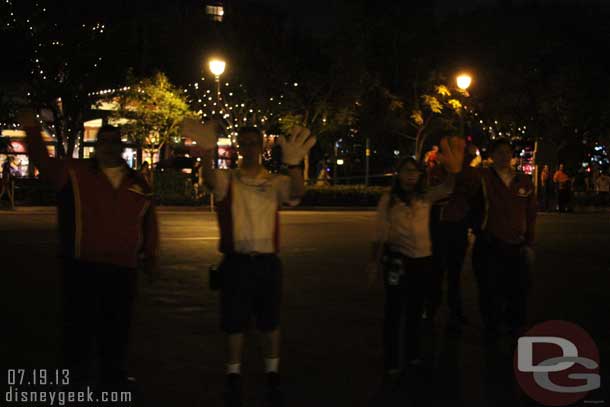 A group of cast members standing in the middle of the tram stop waving to trams.