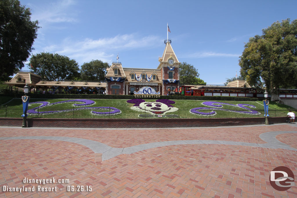 An unobstructed daytime picture of the Main Street Train Station, Floral Mickey and 60th Anniversary signage as the Ward Kimball arrives.