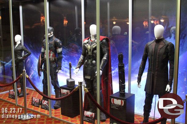 Four Avenger costumes and props in the pre-show waiting area.