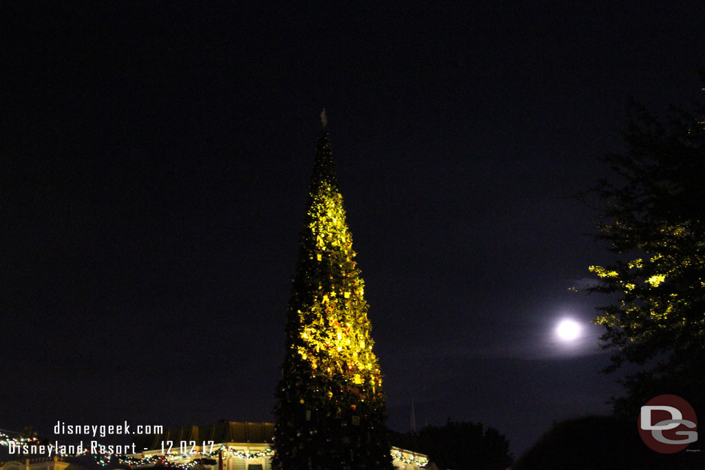 The Christmas tree with the nearly full moon rising and some spot lights hitting it.