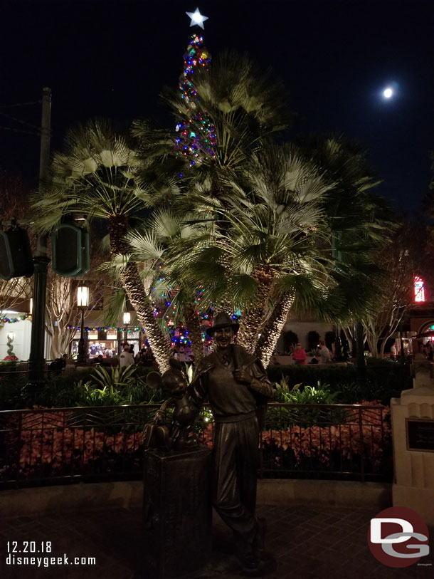 Walt & Mickey Storyteller Statue with Christmas Tree and Moon behind them.