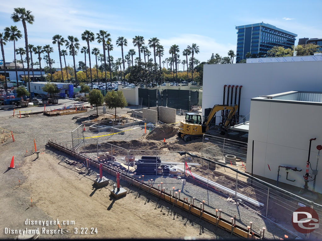 Trees are staged, and some installed in the area behind the buildings.